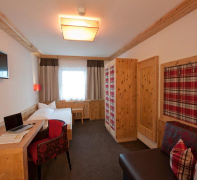 Comfortable room with a single bed, chest, sofa, wooden table with a laptop, a TV and a chair.