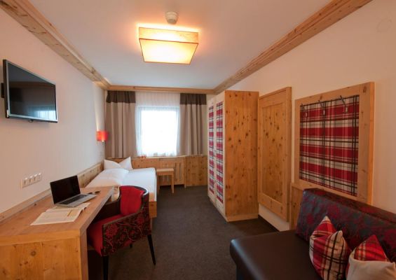 Comfortable room with a single bed, chest, sofa, wooden table with a laptop, a TV and a chair.