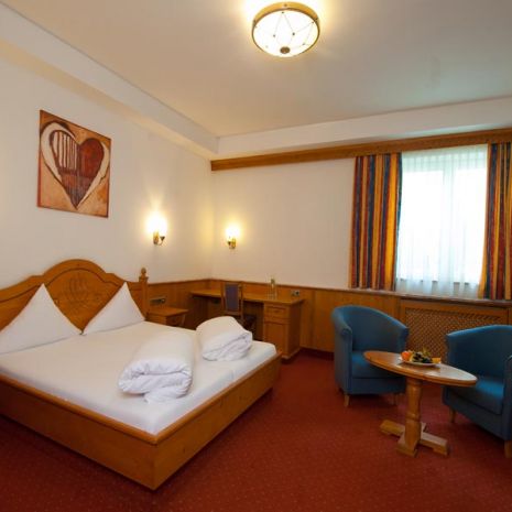The image shows part of a four-bed room at the Hotel Bierwirt. You can see two chairs at a round wooden table, a desk and a double bed, above which hangs a picture with a heart.