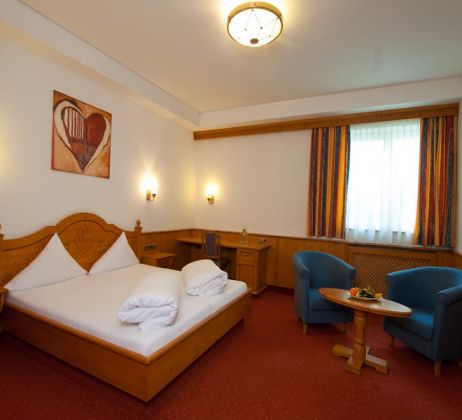 The image shows part of a four-bed room at the Hotel Bierwirt. You can see two chairs at a round wooden table, a desk and a double bed, above which hangs a picture with a heart.